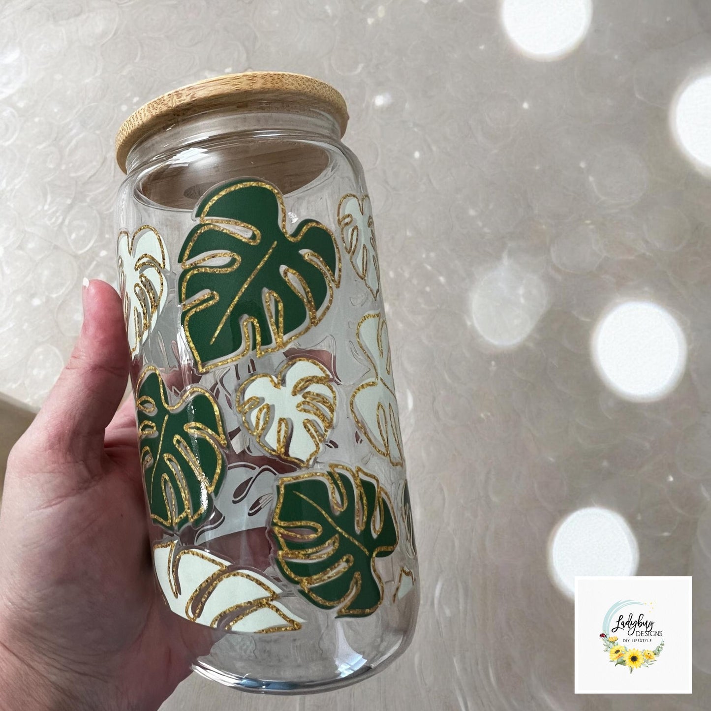 Monstera Leaf Cup with bamboo lid and plastic straw. Features a 16 oz beer can glass design with permanent UV DTF transfer. Perfect for iced coffee and plant lovers. Ideal as a plant mom gift, with hand wash care instructions.