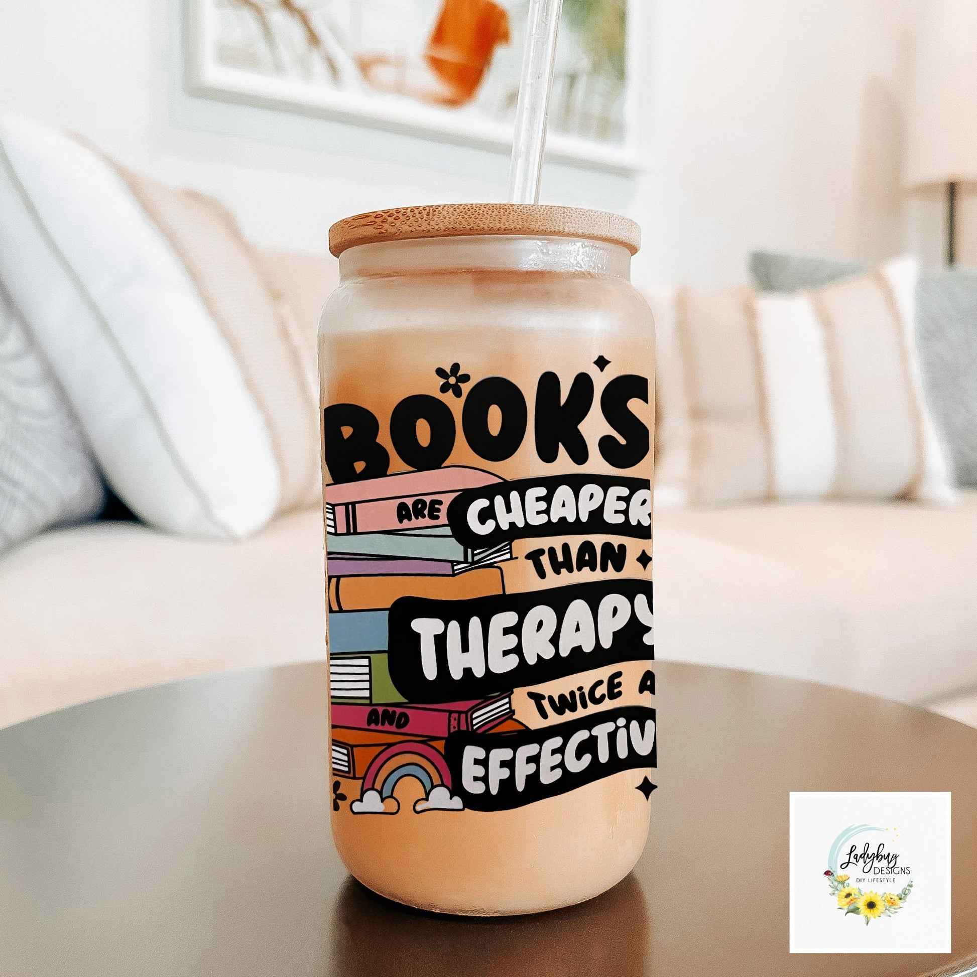 Book are Cheaper than Therapy Glass Can 16oz with Bamboo Lid and Plastic Straw. Ideal for iced coffee and perfect as a book lover&#39;s gift. Shown on a cozy reading table with a book and coffee cup, highlighting its stylish design.